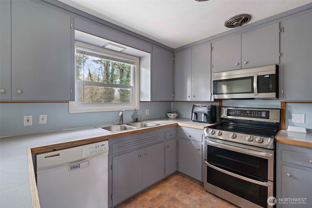 kitchen featuring a sink, light countertops, gray cabinetry, and stainless steel appliances