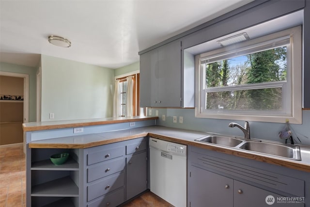 kitchen featuring dishwasher, a peninsula, gray cabinetry, and a sink