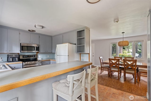 kitchen with open shelves, gray cabinets, stainless steel appliances, light countertops, and a kitchen bar