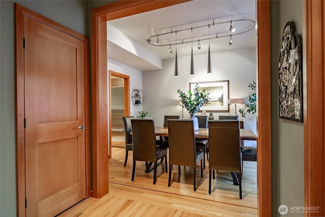 dining space with rail lighting and light wood-style floors