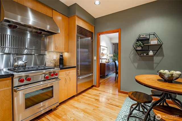 kitchen featuring dark countertops, wall chimney exhaust hood, high quality appliances, and light wood-type flooring