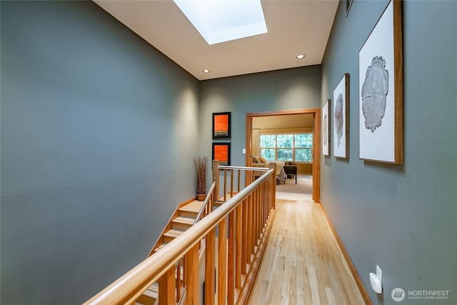 corridor with baseboards, a skylight, recessed lighting, an upstairs landing, and light wood-type flooring