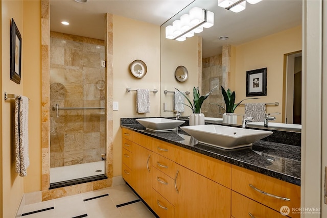 full bath with a sink, a stall shower, double vanity, and tile patterned flooring