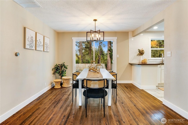 dining space featuring a wealth of natural light, visible vents, wood-type flooring, and an inviting chandelier