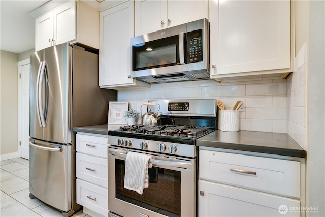 kitchen featuring tasteful backsplash, dark countertops, stainless steel appliances, white cabinets, and light tile patterned floors