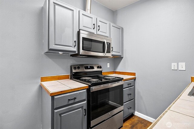 kitchen featuring stainless steel appliances, dark wood-style flooring, gray cabinets, and baseboards