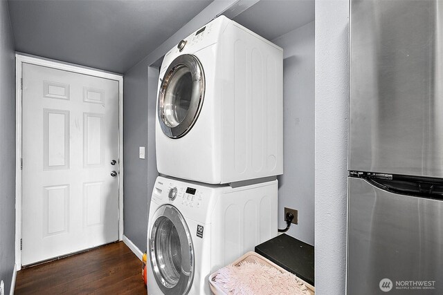 clothes washing area with stacked washer / dryer, dark wood-style flooring, and laundry area