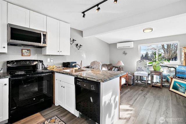 kitchen with wood finished floors, a peninsula, black appliances, a sink, and a wall mounted AC