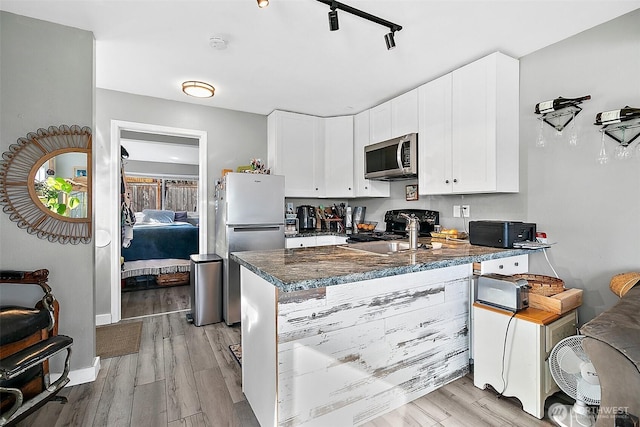 kitchen with stainless steel appliances, a peninsula, white cabinets, light wood-type flooring, and dark stone counters