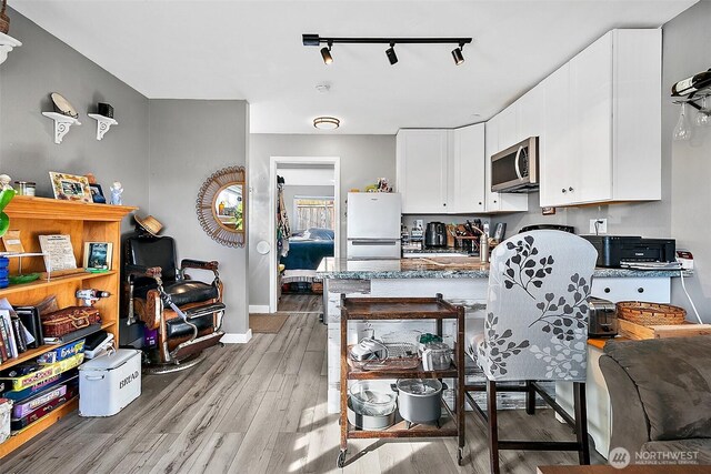 kitchen with white cabinets, light wood-style flooring, stainless steel microwave, freestanding refrigerator, and a peninsula