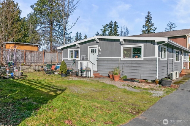 view of front facade with a front lawn, board and batten siding, central AC unit, and fence