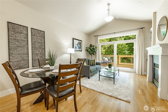 dining room featuring a glass covered fireplace, baseboards, lofted ceiling, and light wood finished floors