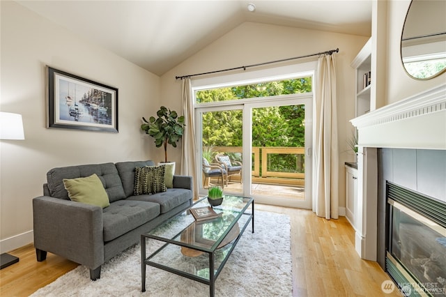 living area featuring vaulted ceiling, light wood-type flooring, a fireplace, and baseboards