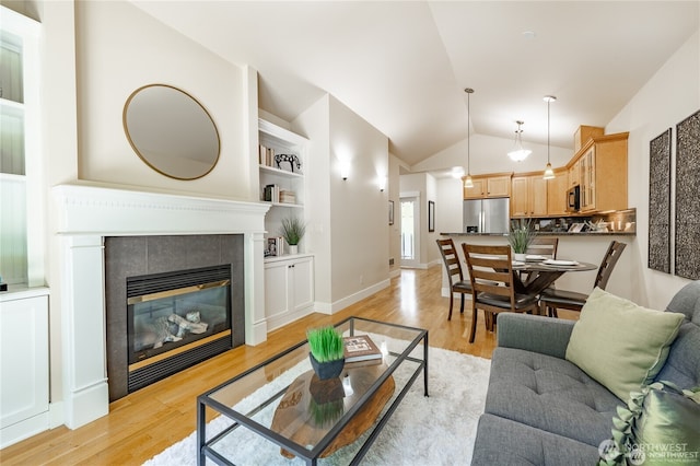 living area with baseboards, lofted ceiling, built in shelves, light wood-style floors, and a fireplace