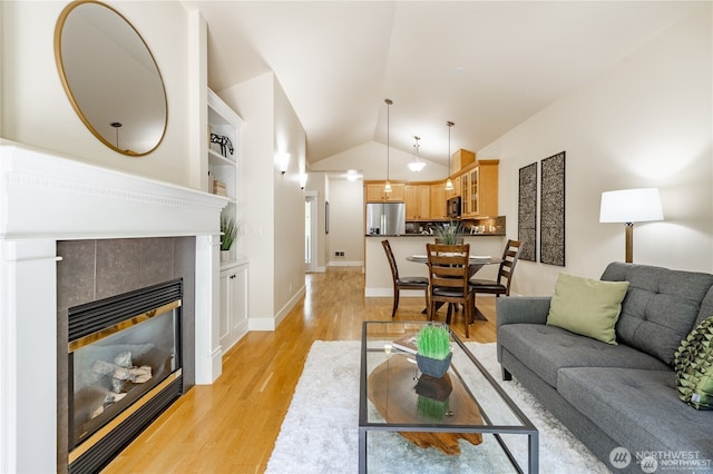 living room with built in shelves, light wood-style flooring, a fireplace, baseboards, and vaulted ceiling