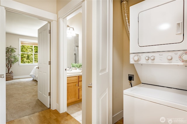 clothes washing area with light carpet, light wood finished floors, stacked washer / dryer, and a sink