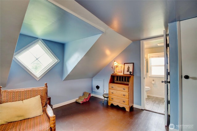 bedroom featuring connected bathroom, vaulted ceiling with skylight, baseboards, and wood finished floors