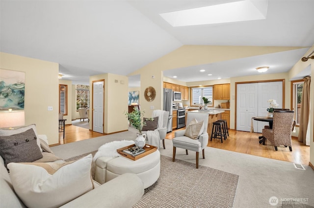 living area featuring vaulted ceiling with skylight, recessed lighting, light wood-style flooring, and visible vents