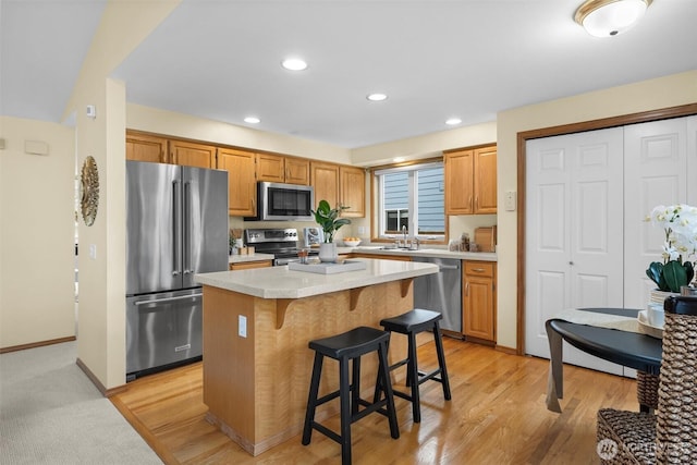 kitchen with a kitchen breakfast bar, a kitchen island, stainless steel appliances, light wood finished floors, and light countertops