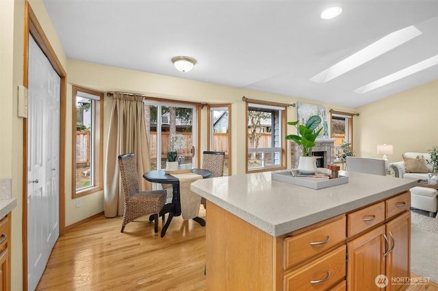 kitchen featuring a kitchen island, light wood-style flooring, a fireplace, light countertops, and open floor plan