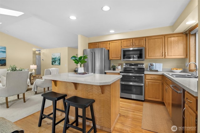 kitchen featuring light wood-style flooring, a sink, light countertops, appliances with stainless steel finishes, and a kitchen bar