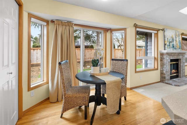 dining room featuring baseboards, a brick fireplace, and light wood-style flooring