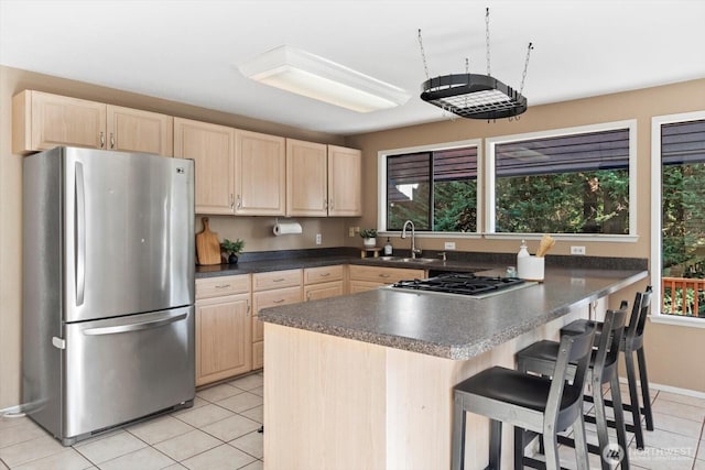 kitchen featuring dark countertops, light brown cabinets, a breakfast bar area, and stainless steel appliances