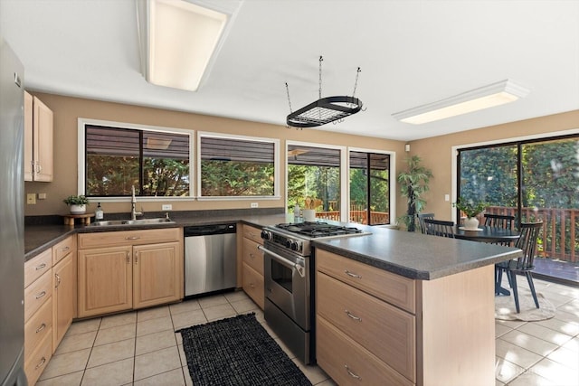 kitchen with dark countertops, appliances with stainless steel finishes, a peninsula, light brown cabinets, and a sink