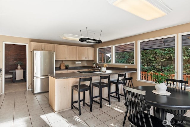 kitchen featuring light tile patterned floors, light brown cabinetry, dark countertops, and freestanding refrigerator