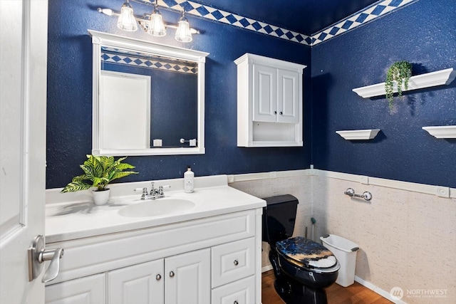 bathroom with a textured wall, toilet, wood finished floors, vanity, and wainscoting