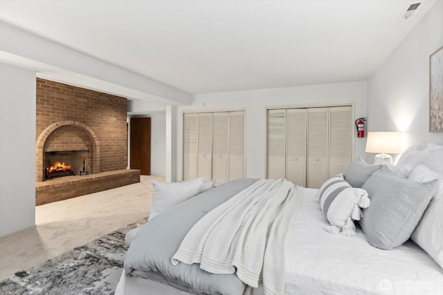 bedroom featuring carpet floors, a brick fireplace, visible vents, and two closets