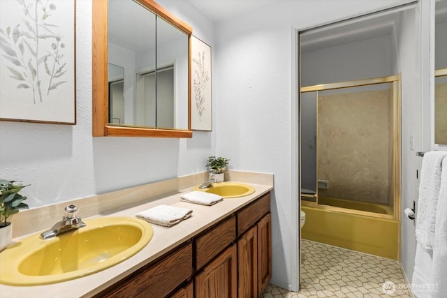 bathroom featuring bath / shower combo with glass door, a sink, toilet, and double vanity