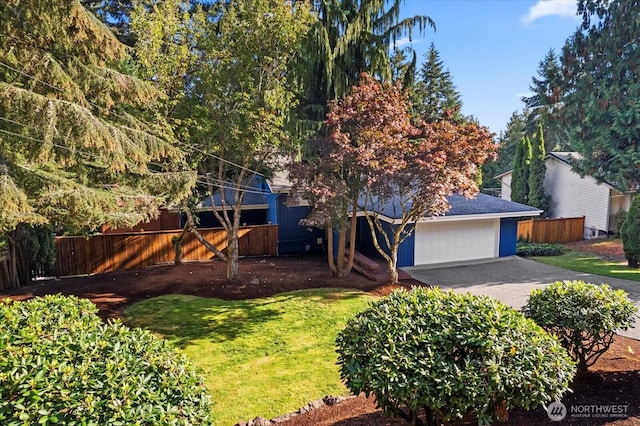 view of property hidden behind natural elements with a garage, driveway, fence, and a front yard