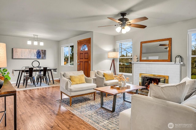 living room with ceiling fan with notable chandelier, a fireplace, baseboards, and hardwood / wood-style floors