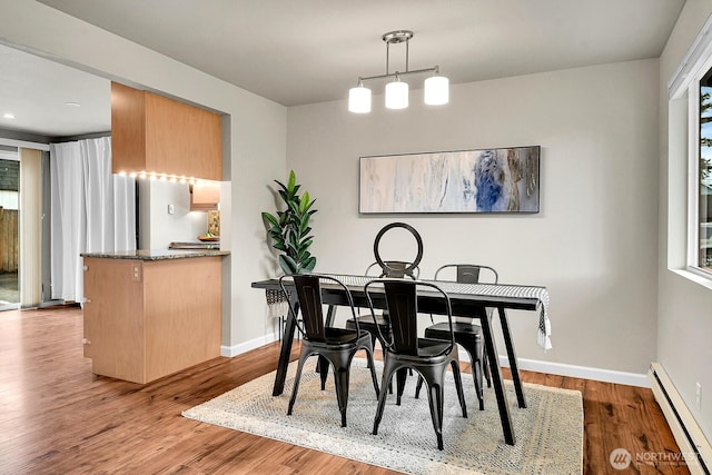 dining space with a baseboard heating unit, wood finished floors, and baseboards