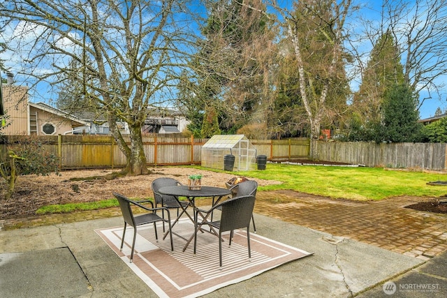 view of patio with a greenhouse, a fenced backyard, outdoor dining area, and an outdoor structure