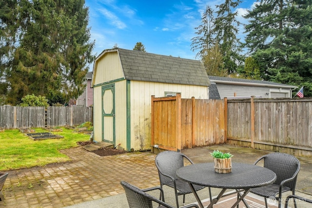 view of patio / terrace with a fenced backyard, a garden, an outbuilding, outdoor dining space, and a storage unit