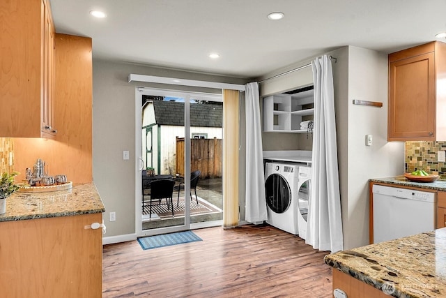 kitchen featuring washing machine and dryer, light wood-type flooring, light stone counters, decorative backsplash, and white dishwasher