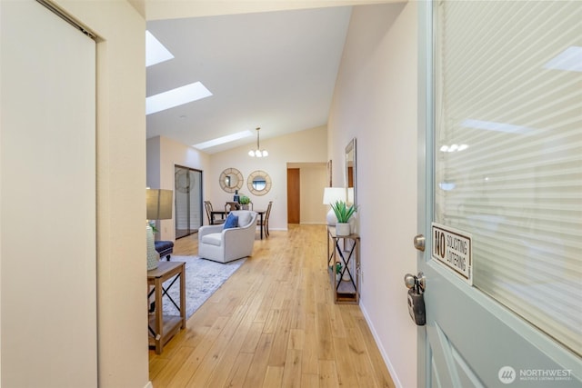 hallway with lofted ceiling with skylight, a notable chandelier, light wood-type flooring, and baseboards