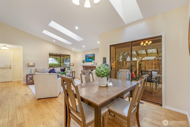 dining space featuring light wood-type flooring, recessed lighting, vaulted ceiling with skylight, a fireplace, and baseboards