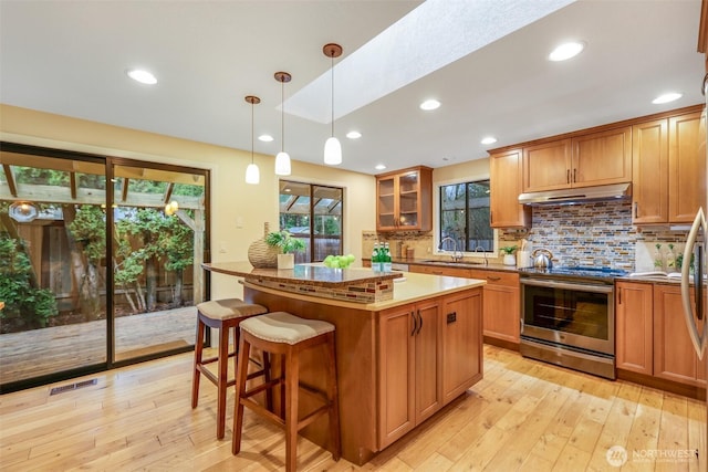 kitchen featuring a kitchen island, under cabinet range hood, stainless steel electric range oven, decorative backsplash, and a sink