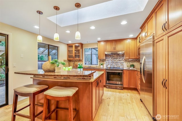 kitchen with a center island, glass insert cabinets, dark stone counters, stainless steel appliances, and a sink