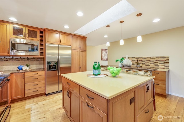 kitchen featuring a skylight, backsplash, light wood-style floors, and built in appliances