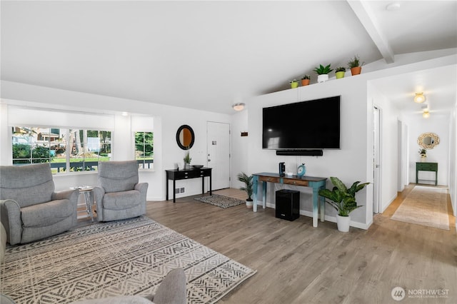 living room featuring vaulted ceiling with beams, light wood-style floors, and baseboards