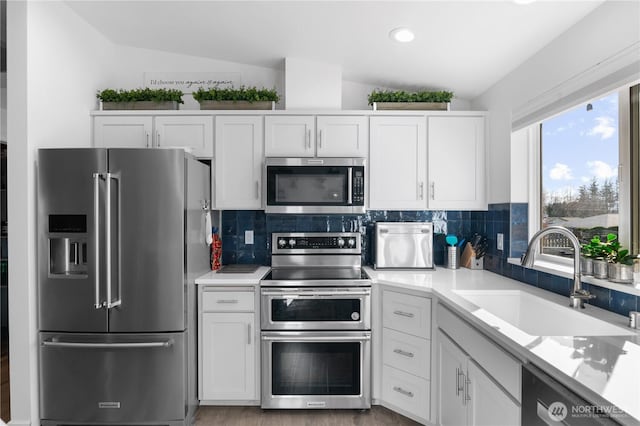 kitchen with lofted ceiling, white cabinets, appliances with stainless steel finishes, and a sink