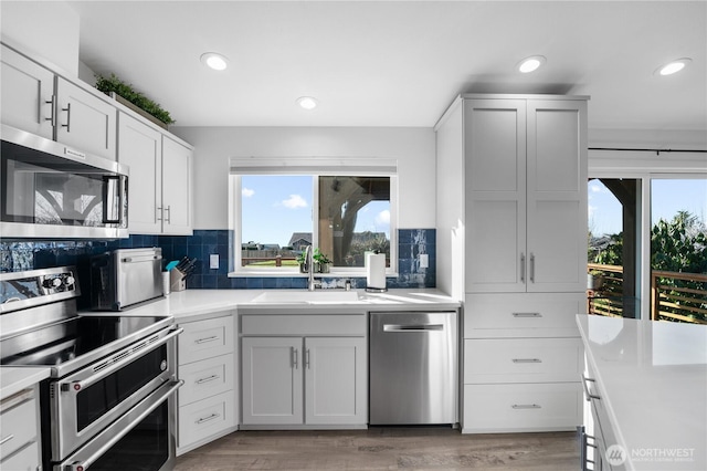 kitchen with light wood-style flooring, a sink, tasteful backsplash, appliances with stainless steel finishes, and light countertops