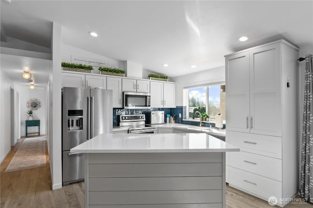 kitchen featuring backsplash, a center island, stainless steel appliances, light countertops, and vaulted ceiling