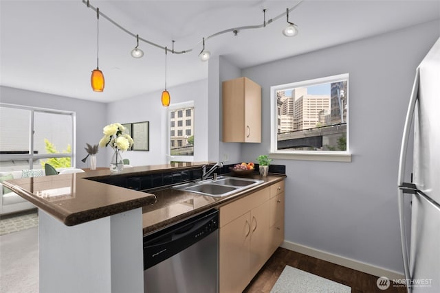 kitchen featuring dishwasher, dark countertops, a peninsula, a healthy amount of sunlight, and a sink