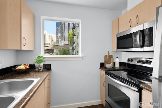 kitchen featuring dark countertops, light brown cabinets, appliances with stainless steel finishes, and a sink