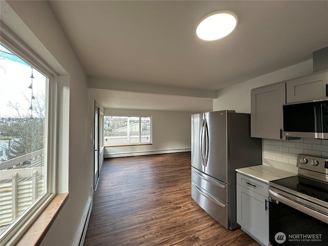 kitchen featuring light stone counters, dark wood finished floors, decorative backsplash, baseboard heating, and appliances with stainless steel finishes